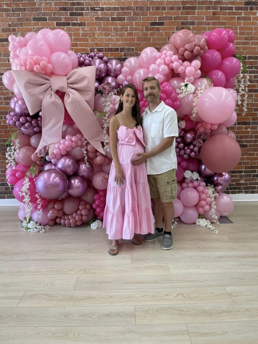 husband and wife standing in front of pink balloon wall