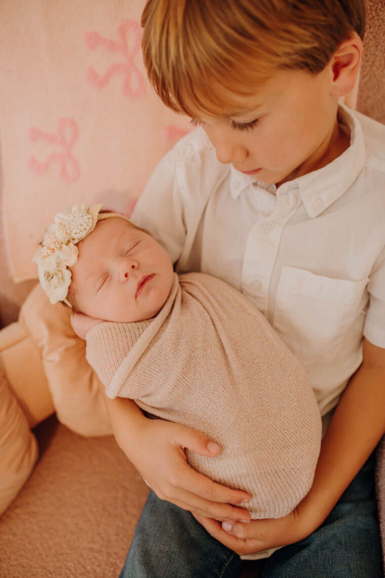 big brother holding newborn baby sister looking at her